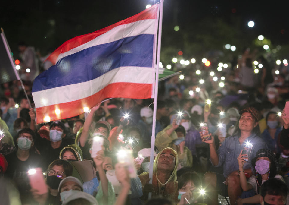 Pro-democracy protesters wave a flag and hold up lights during a protest at Sanam Luang in Bangkok, Thailand, Saturday, Sept. 19, 2020. Thousands of demonstrators turned out Saturday for a rally to support the student-led protest movement's demands for new elections and reform of the monarchy. (AP Photo/Wason Wanichakorn)