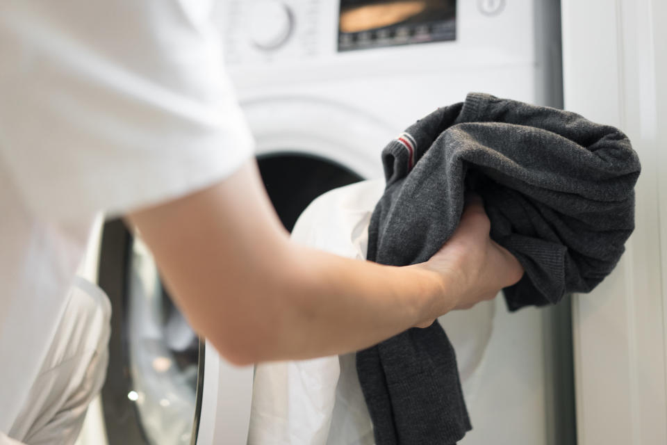 Someone puts clothes in a washing machine