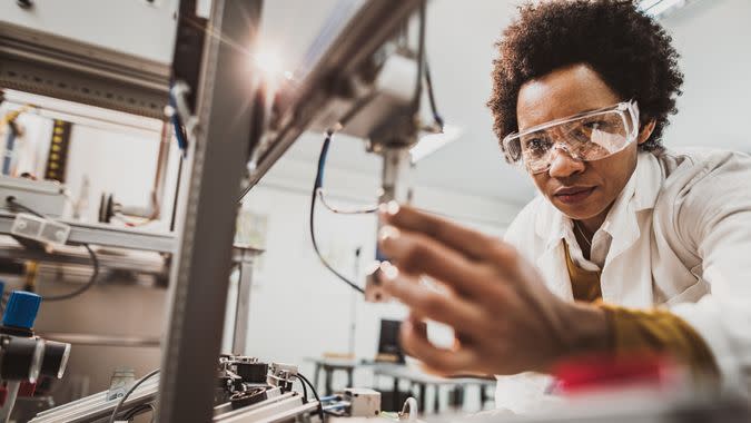 Low angle view of African American lab worker examining machine part while working in a lab.