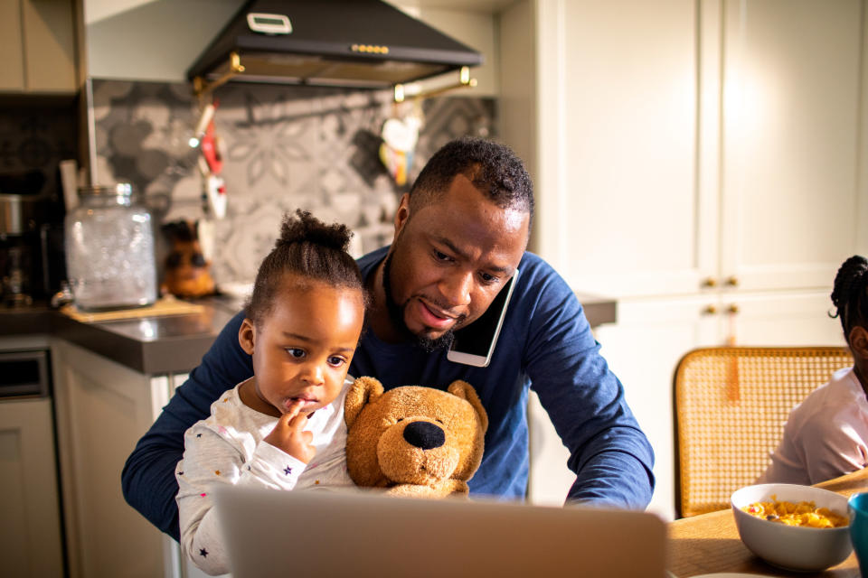 a dad works from home with his daughter on his lap