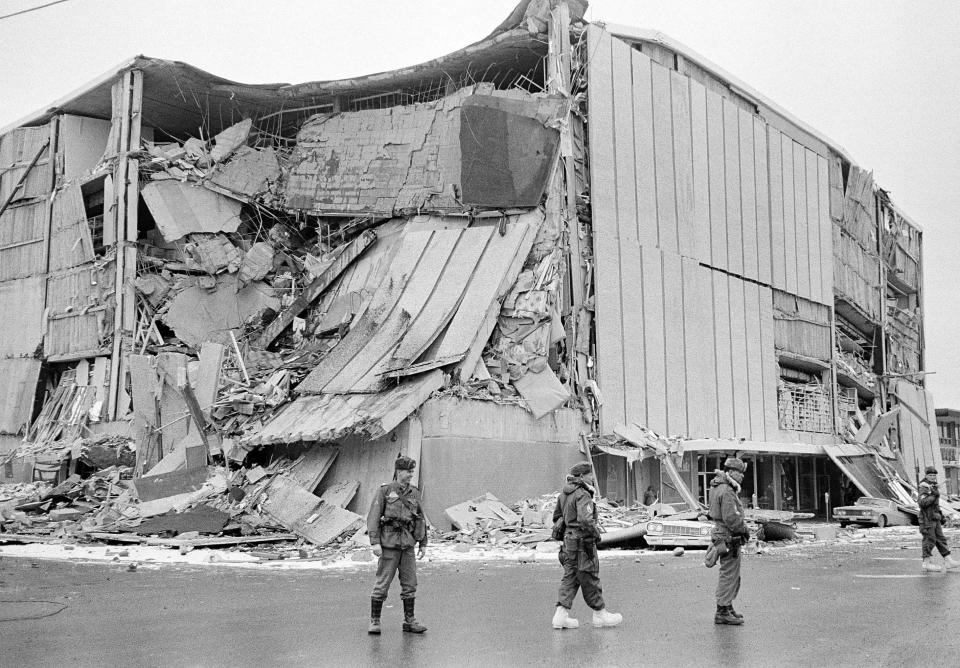 File - In this March 28, 1964 file photo, with the city under martial law, soldiers patrol a downtown street in Anchorage, Alaska. In bacground is the wreckage of the five-story Penney store at Fifth Avenue and D Street. North America's largest earthquake rattled Alaska 50 years ago, killing 15 people and creating a tsunami that killed 124 more from Alaska to California. The magnitude 9.2 quake hit at 5:30 p.m. on Good Friday, turning soil beneath parts of Anchorage into jelly and collapsing buildings that were not engineered to withstand the force of colliding continental plates. (AP Photo/File)