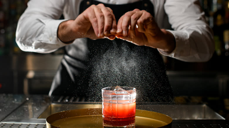 Bartender spraying lemon on cocktail 