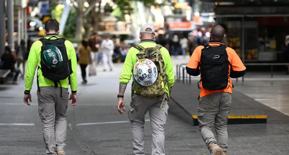 Three tradesmen walking down the street with backpacks on.