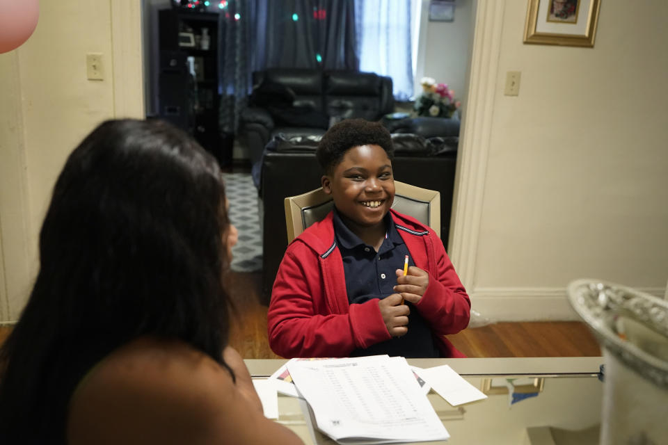 Evena Joseph, left, sits with her son J. Ryan Mathurin, 9, right, as he smiles while doing his homework, Thursday, Dec. 22, 2022, at their home, in Boston. (AP Photo/Steven Senne)