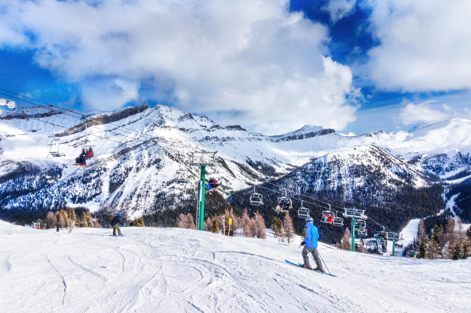 Unidentifiable skiers and snowboarders on chairlift going up a ski slope in the snowy mountain range of the Canadian Rockies.