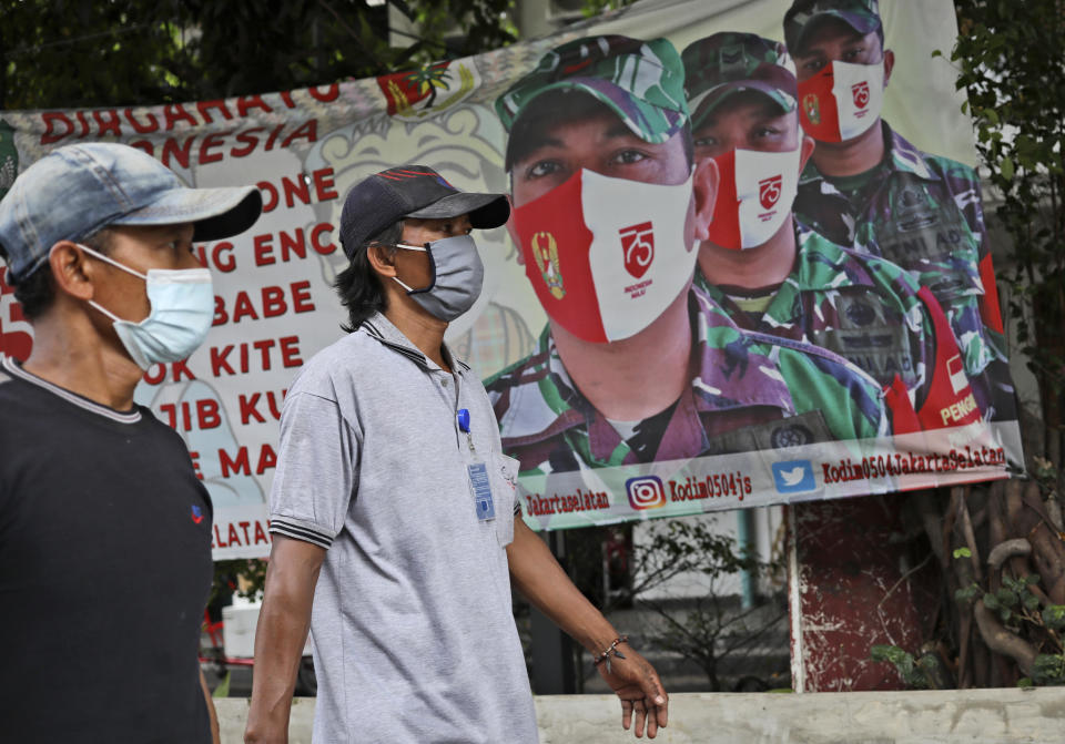 Indonesian men walk past a banner put up by Indonesian Army calling for people to always have their mask on to prevent the spread of coronavirus outbreak in Jakarta, Indonesia, Thursday, Dec. 17, 2020. (AP Photo/Dita Alangkara)