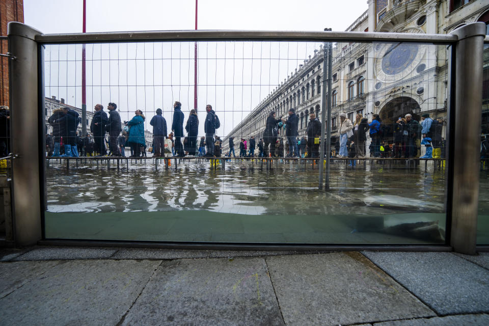 Tourists and residents walk on catwalks during a sea tide of around 97 centimeters (38.18 inches) to cross a flooded St. Mark's Square in Venice, northern Italy, Saturday, Dec. 10, 2022, where recently installed glass barriers prevent seawater from flooding the 900-year-old iconic St Mark's Basilica. St. Mark's Square is the lowest-laying city area and frequently ends up underwater during extreme weather. (AP Photo/Domenico Stinellis)
