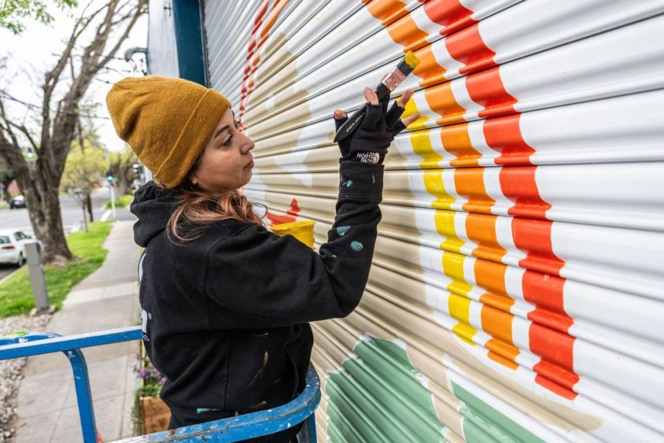 Uli Smith, a Sacramento artist, paints a mural at a business on 19th Street on Wednesday. She began working with Wide Open Walls in 2022. Hector Amezcua/hamezcua@sacbee.com