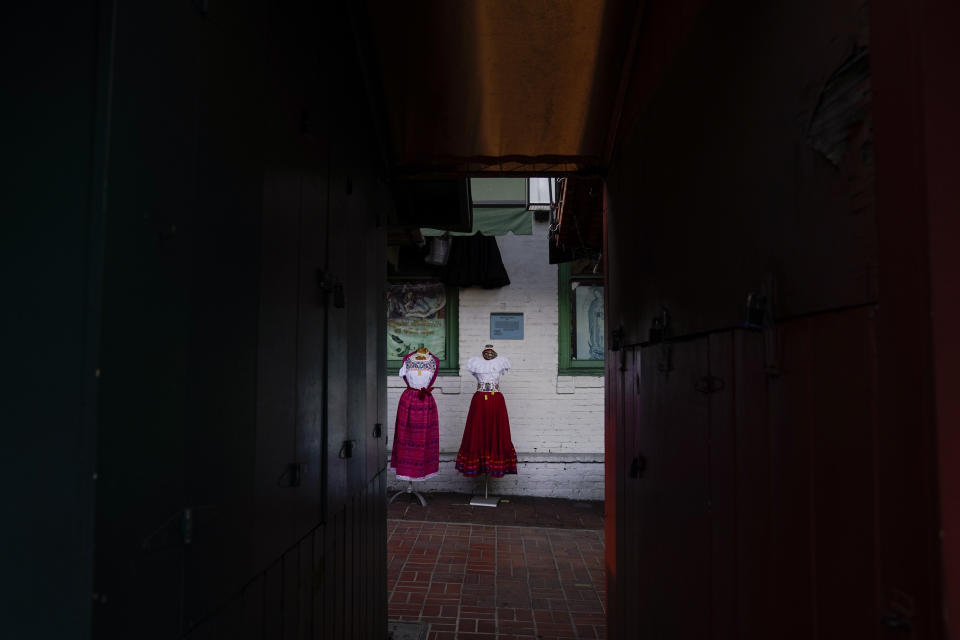 Traditional Mexican folk dresses are seen between shuttered market stalls on Olvera Street in downtown Los Angeles, Tuesday, Dec. 15, 2020. The tree-covered brick alley typically teeming with tourists is empty. Many of the shops that sell everything from traditional Mexican folk dresses to paintings of artist Frida Kahlo to sombreros are padlocked and the ones open have few, if any, customers. (AP Photo/Jae C. Hong)