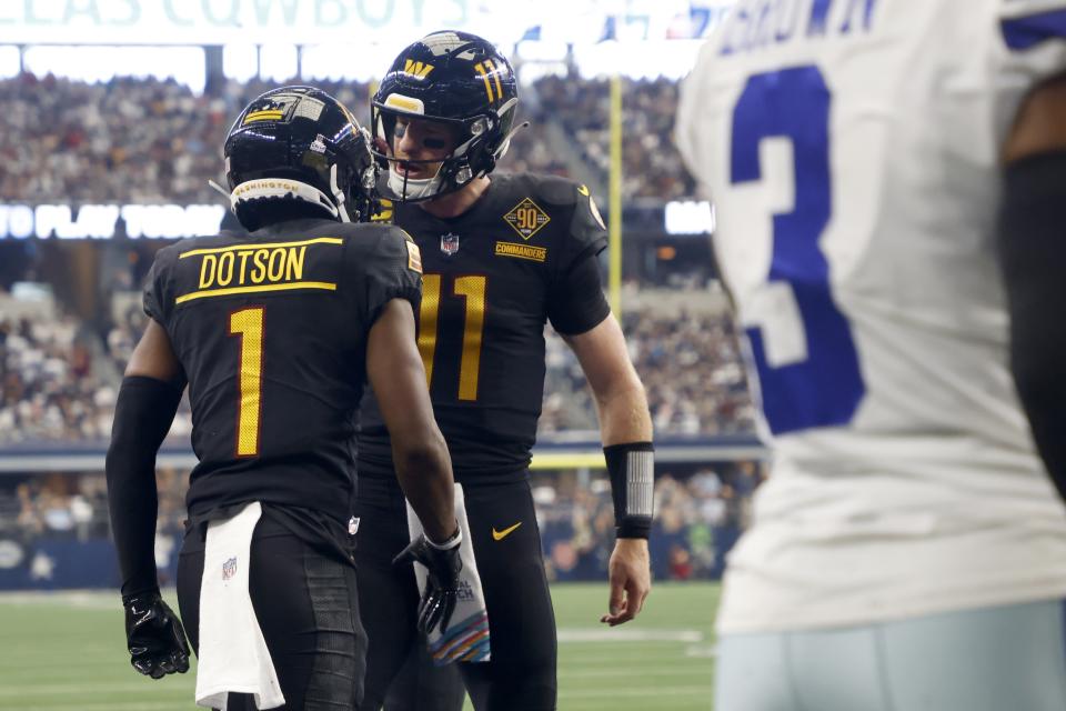 Washington Commanders' Jahan Dotson (1) and Carson Wentz (11) celebrate after Dotson caught a touchdown pass as Dallas Cowboys cornerback Anthony Brown (3) walks past in the first half of a NFL football game in Arlington, Texas, Sunday, Oct. 2, 2022. (AP Photo/Michael Ainsworth)