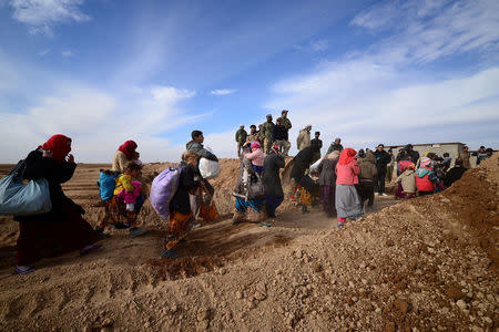 Displaced people, fleeing the violence of Islamic State militants in outskirts of Sinjar, walk past Shiite fighters in Sinjar, Iraq, December 5, 2016. REUTERS/Stringer