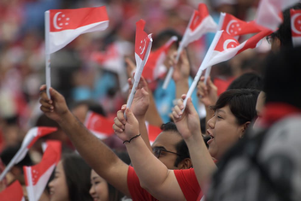 Spectators wave the Singapore national flag as they wait for the start of the 54th National Day Parade in Singapore August 9, 2019. — AFP pic