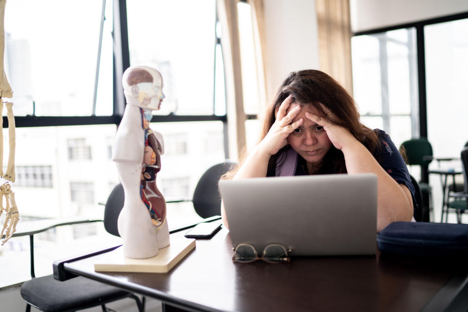 A stressed person holding their head in their hands as they look at their laptop