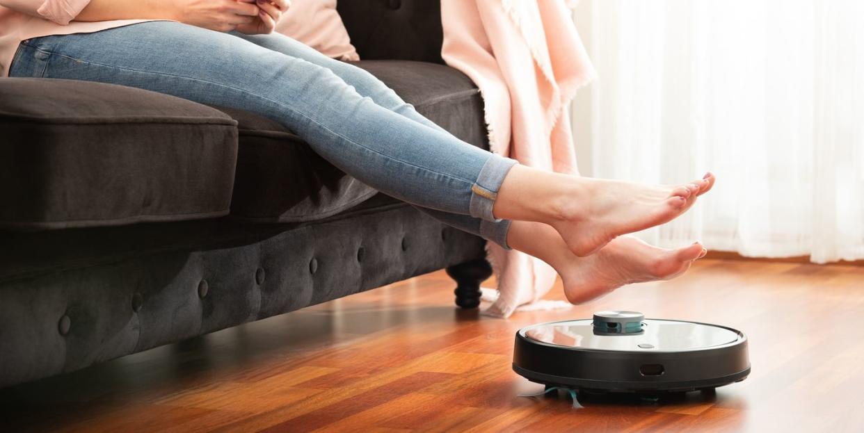 low section of woman sitting on sofa with robotic vacuum cleaner at home