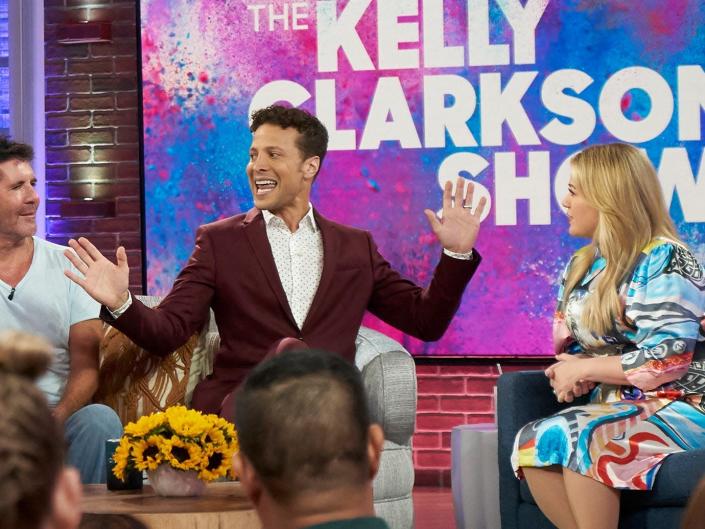 Randy Jackson, Paula Abdul, Simon Cowell, and Justin Guarini sit on a couch in front of Kelly Clarkson next to sign with &quot;The Kelly Clarkson Show&quot; text