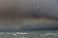 A man kitesurfs near the shores of the city of Chalkida as smoke rises from a wildfire burning on the island of Evia