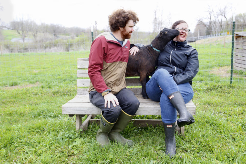 A goat sniffs Alison Dreith's face, as her husband, Jake McDaniel, watches on Wednesday, April 13, 2022, at their southern Illinois farm. Dreith works remotely for the Midwest Access Coalition, which pays for "practical support" for women seeking abortions. That includes things like air fare, gas money, hotel rooms or child care. She says McDaniel sometimes lends a hand, picking up out-of-state clients at the St. Louis airport and driving them to clinics in Illinois, one of a few states that are quickly becoming abortion hubs as others restrict abortion access. (AP Photo/Martha Irvine)