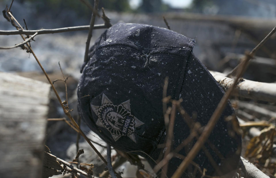 The cap of a Michoacan state police officer lies in the brush where charred police trucks stand on the roadside after its police officer occupants were attacked in El Aguaje, Mexico, Monday, Oct. 14, 2019. At least 13 police officers were killed and three others injured Monday in the ambush. (AP Photo/Armando Solis)