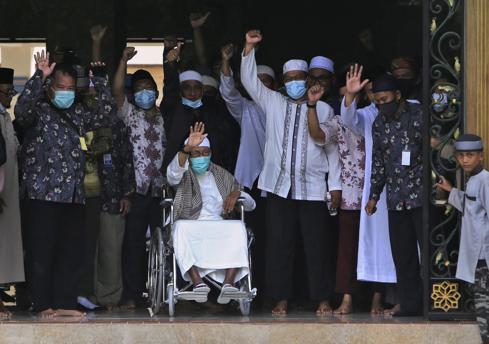 Islamic cleric Abu Bakar Bashir, center, waves from a wheelchair upon arrival at the Al Mukmin Islamic Boarding School where he resides in Solo, Central Java, Indonesia, Friday, Jan. 8, 2021. The firebrand cleric who inspired the Bali bombers and other violent extremists walked free from prison Friday after completing his sentence for funding the training of Islamic militants. (AP Photo/Moh. Sulistyo)