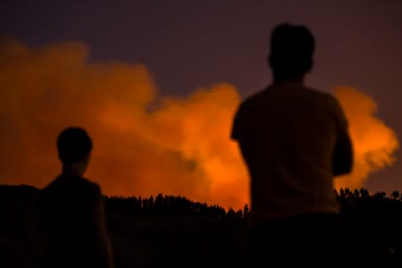 Two people look at flames and smoke from a forest fire, seen in the village of Valleseco