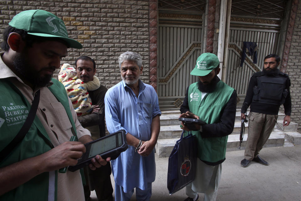 A police officer, right, stands guard as government workers collect data from men during census, in Peshawar, Pakistan, Wednesday, March 1, 2023. Pakistan on Wednesday launched its first-ever digital population and housing census to gather demographic data on every individual ahead of the parliamentary elections which are due later this year, officials said. (AP Photo/Muhammad Sajjad)