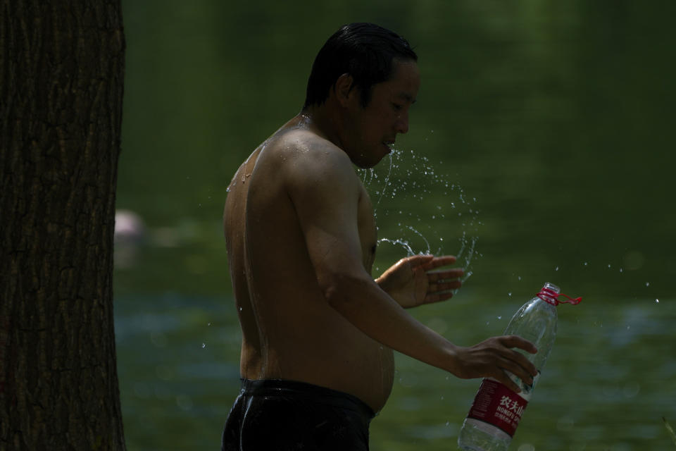 A resident tosses water to cool off on a sweltering day at an urban waterway in Beijing, Monday, July 10, 2023. Rescuers were looking Monday for several people missing in a landslide triggered by torrential rains while employers across much of China were ordered to limit outdoor work due to scorching temperatures as the country struggled with heat, flooding and drought. (AP Photo/Andy Wong)