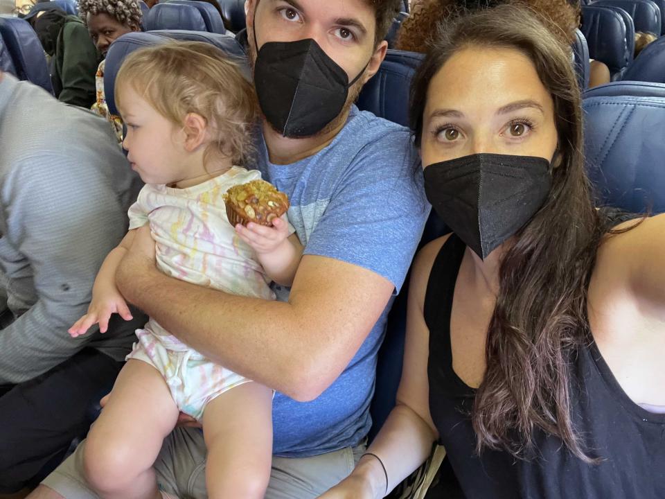 A family of 3 with parents and a baby taking a selfie on a plane wearing masks.