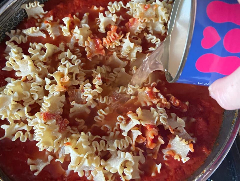 A pan of noodles and sauce with seasoning poured on top.