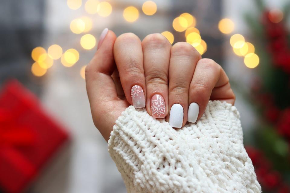 idea of the winter manicure womans hand with gel polish manicure white color and with snowflakes ornament against festive christmas background selective focus