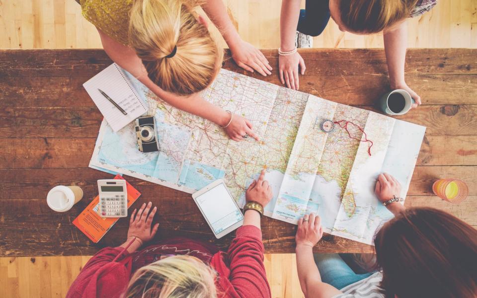Friends using a map to plan a holiday - Getty