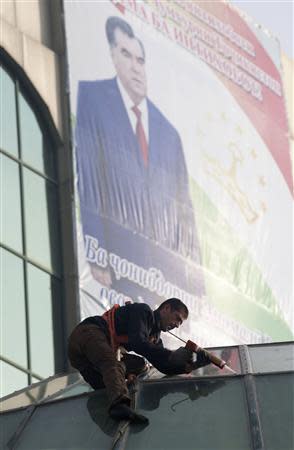 An employee works on a roof, with a billboard displaying Tajikistan's President Imomali Rakhmon seen in the background, in Dushanbe, November 1, 2013. REUTERS/Nozim Kalandarov