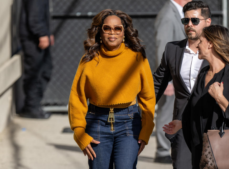 Oprah Winfrey in a sweater and sunglasses, walking with her team