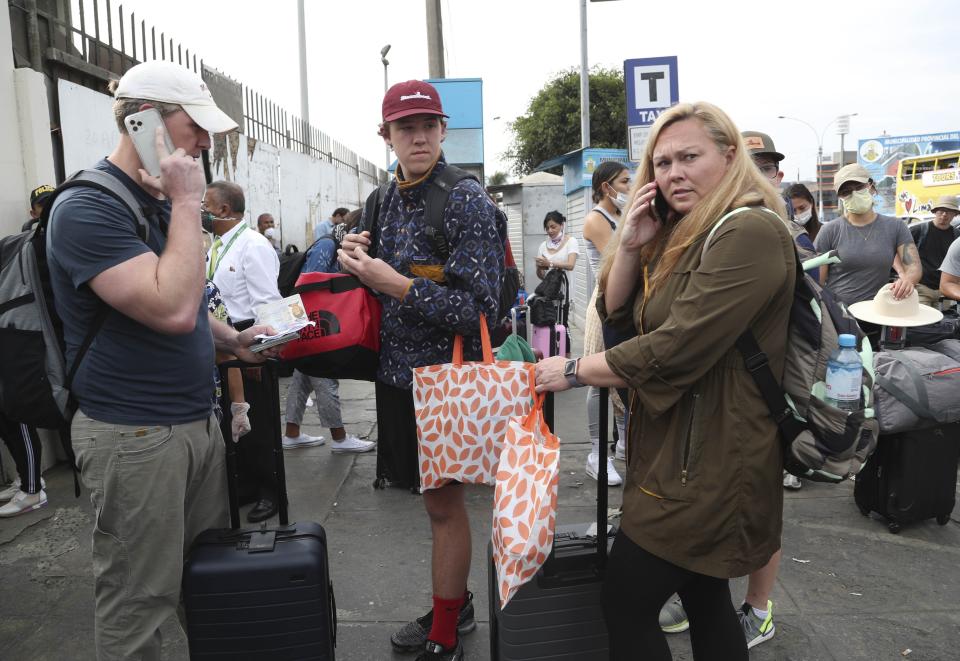 Tourists from the United States wait outside the closed Jorge Chavez International Airport for a member of the U.S. Embassy to escort them to a flight that will fly them back to the U.S., in Callao Peru, Friday, March 20, 2020, on the fifth day of a state of emergency decreed by the government to prevent the spread of the new coronavirus. (AP Photo/Martin Mejia)