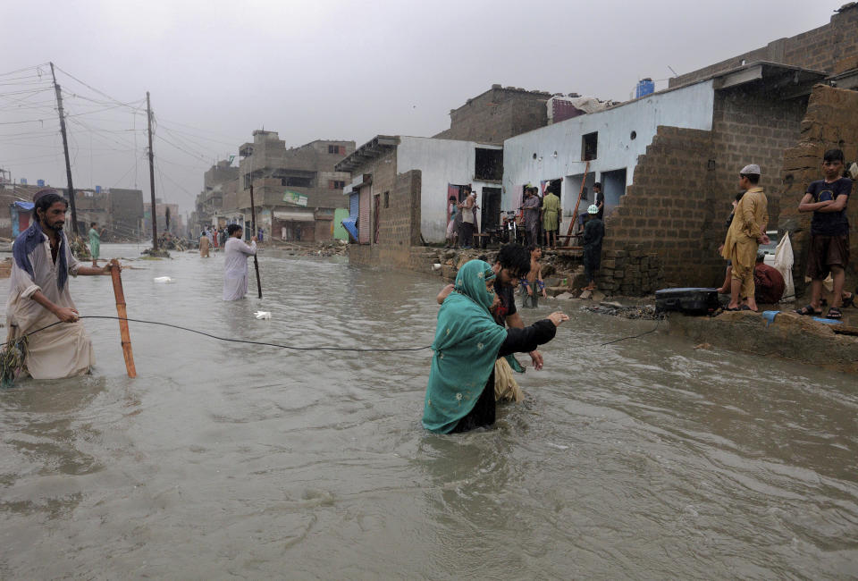 Local residents wade through a flooded street during a heavy monsoon rain in Yar Mohammad village near Karachi, Pakistan, Thursday, Aug. 27, 2020. Pakistan's military said it will deploy rescue helicopters to Karachi to transport some 200 families to safety after canal waters flooded the city amid monsoon rains. (AP Photo/Fareed Khan)