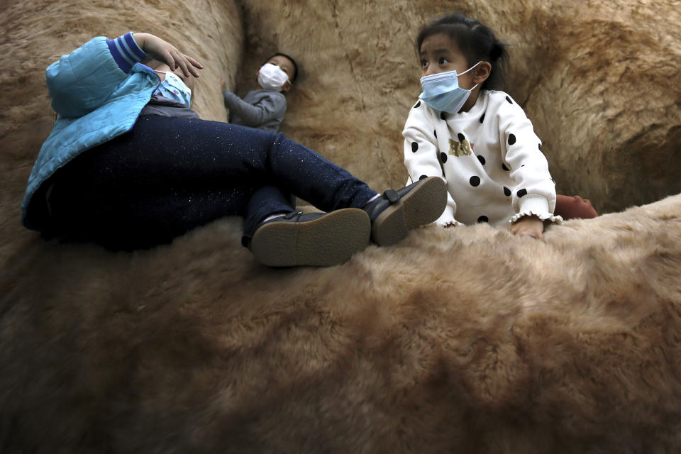 Children wearing face masks to help curb the spread of the coronavirus play on a giant cat structure on display at a commercial office building in Beijing, Sunday, Oct. 18, 2020. (AP Photo/Andy Wong)