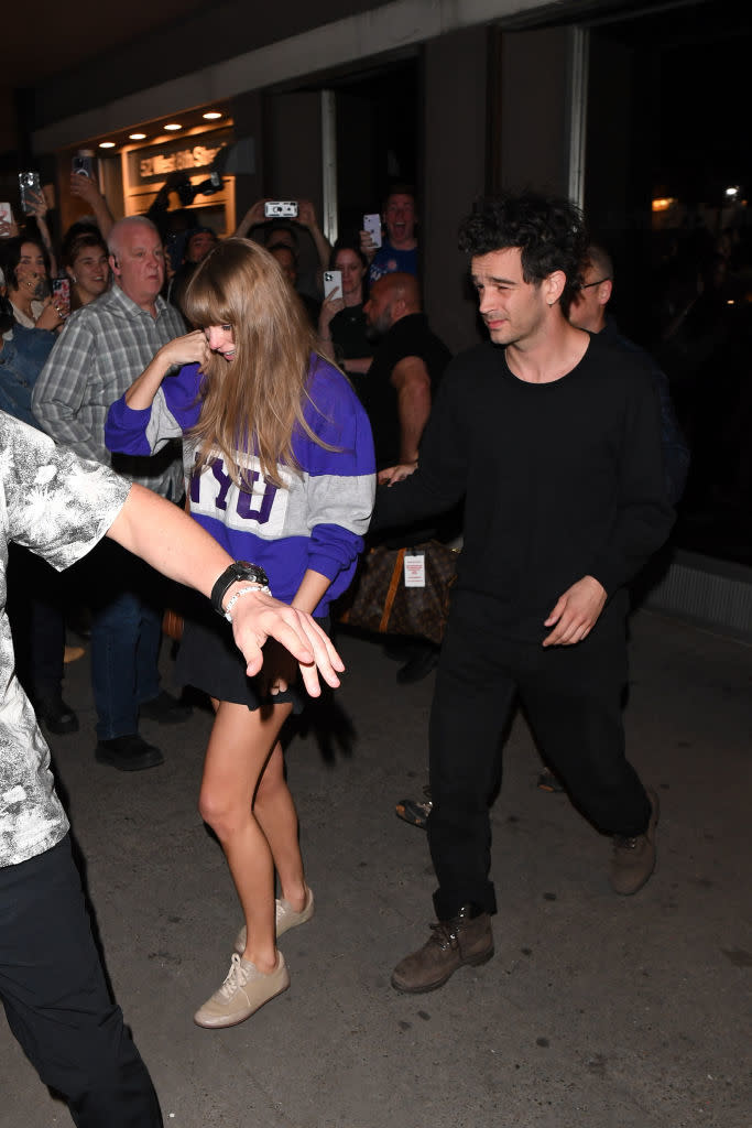 Two individuals, one in a sports jersey and shorts, the other in a black shirt and pants, walking amidst a crowd