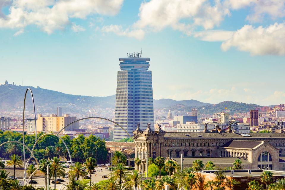 A wide view of palm trees in front of buildings and mountains in Barcelona.