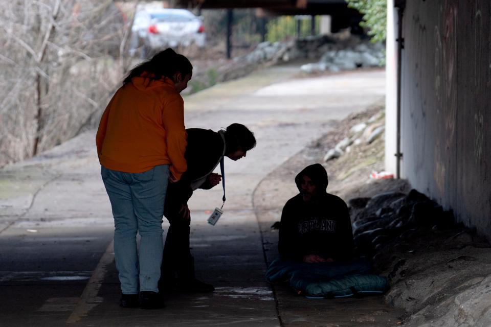 Members of the Resiliency Empowerment Support Team (REST) Letha Croff, left, and Torie Baxter, second from left, talk to a homeless person sleeping under a bridge in Chico, Calif., Feb. 8, 2024. Butte County officials fear the REST program would lose its funding if California voters approve Proposition 1.