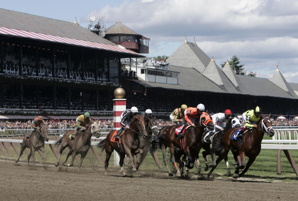 FILE- In this Aug. 18, 2007 file photo, horses race into through the first turn at Saratoga Race Course in Saratoga Springs, N.Y. Saratoga Springs' racetrack is still going strong as it marks its 150th anniversary this summer, the centerpiece attraction in a town that's also known for mineral springs, Victorian charm and upscale hotels, shops and restaurants. (AP Photo/Mike Groll, File)