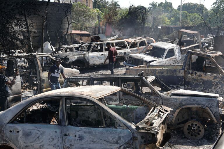 Varias personas buscan piezas rescatables de autos quemados en un taller mecánico incendiado durante la violencia desatada por pandillas armadas en Puerto Príncipe, Haití, el lunes 25 de marzo de 2024. 