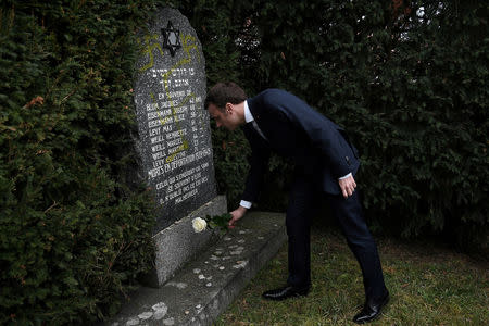 French President Emmanuel Macron lays a white rose on a grave vandalised with swastikas during a visit at the Jewish cemetery in Quatzenheim, France February 19, 2019. Frederick Florin/Pool via REUTERS
