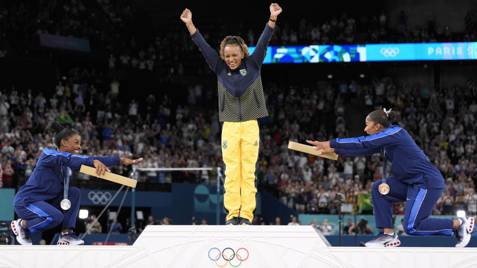 Silver medalist Simone Biles of the United States, left, and bronze medalist Jordan Chiles of the United States, right, bow to gold medalist Rebeca Andrade of Brazil during the medal ceremony for the women's individual floor exercise final at the Bercy Arena during the 2024 Summer Olympics, Monday, Aug. 5, 2024, in Paris, France. (AP Photo/Abbie Parr)