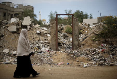 A Palestinian woman walks past the frame of a doorway of a destroyed house, on which British street artist Banksy painted an image of a goddess holding her head in her hand, after the door with the painted image was sold in the northern Gaza Strip April 1, 2015. REUTERS/Mohammed Salem