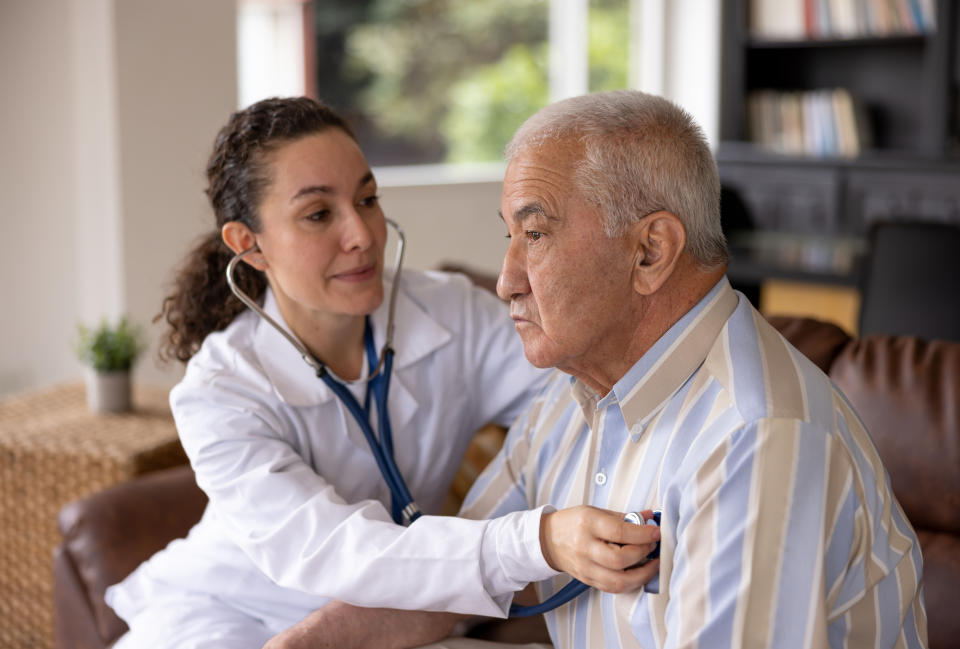 Latin American doctor examining a senior man on a house call and listening to his heart - healthcare and medicine concepts