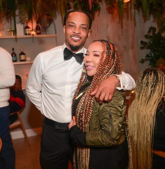 Tip "T.I." Harris in formal wearing with his arm around Tameka Harris with long braids and a olive green bomber jacket