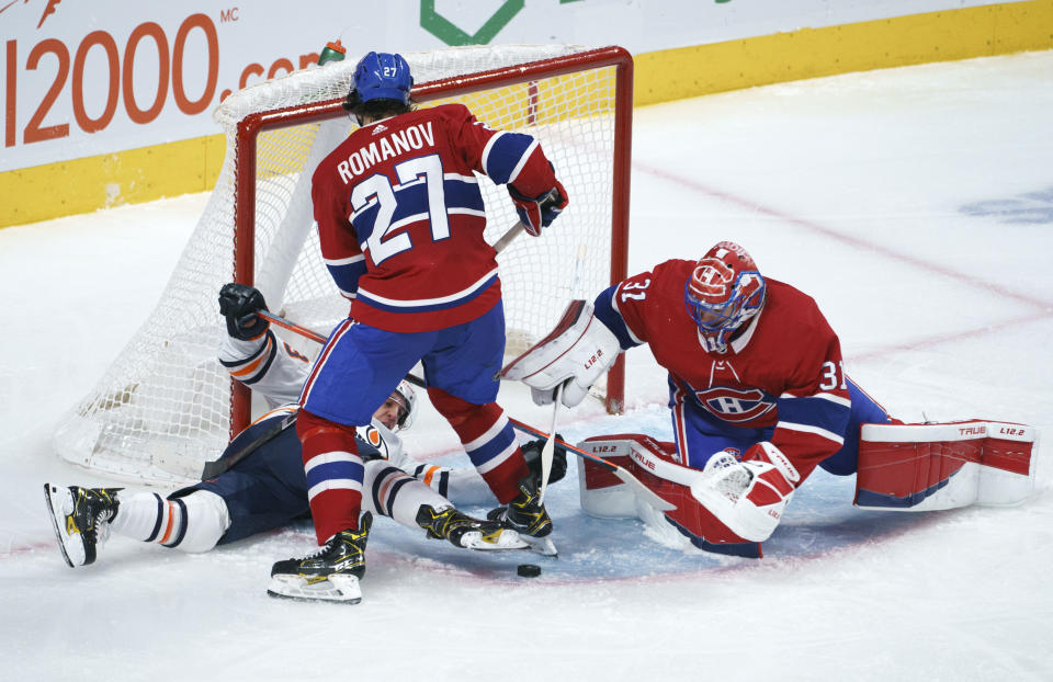 The puck is out of reach for Edmonton Oilers' Tyler Ennis as he is taken out by Montreal Canadiens defenseman Alexander Romanov in front of goaltender Carey Price during the second period of an NHL hockey game, Tuesday, March 30, 2021 in Montreal. (Paul Chiasson/The Canadian Press via AP)