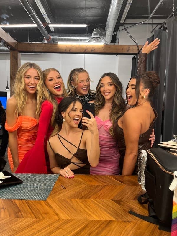 Several former cast members from the show Dance Moms posing joyfully backstage and taking a selfie