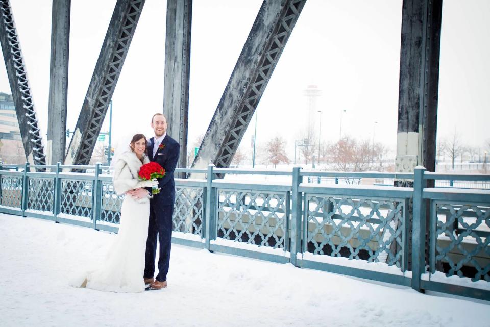 Katie and Nick in their wedding clothes on a snowy bridge.