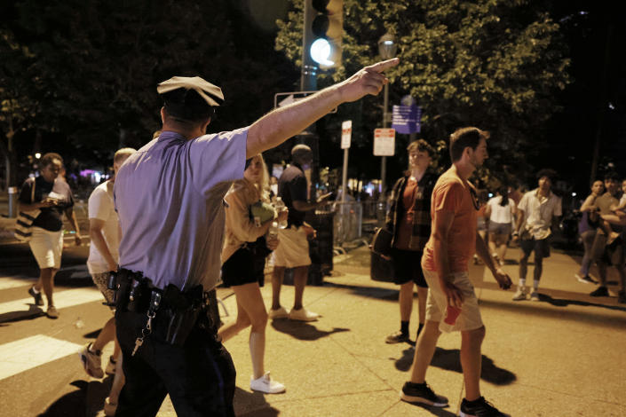 A policeman directs pedestrians at an intersection in the evening.