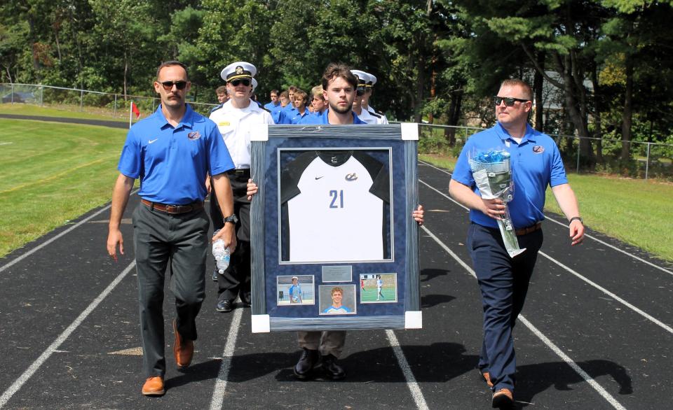 Members of the Maine Maritime men's soccer team march down the track at York High on Saturday, led by head coach Billy Shannon (right), to begin the ceremony to retire Brian Kenealy's No. 21.